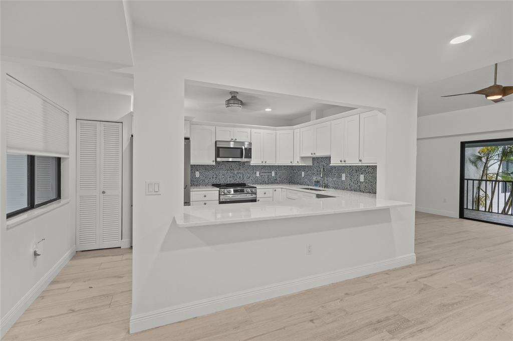 A white kitchen with a breakfast bar overlooks a living area with wood-look flooring — 1508 PELICAN COVE ROAD UNIT 235, SARASOTA, FL