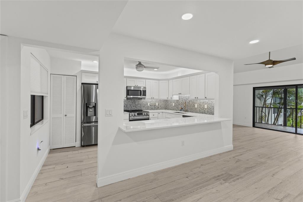 A modern kitchen with white cabinets and a breakfast bar opens into a living area — 1508 PELICAN COVE ROAD UNIT 235, SARASOTA, FL