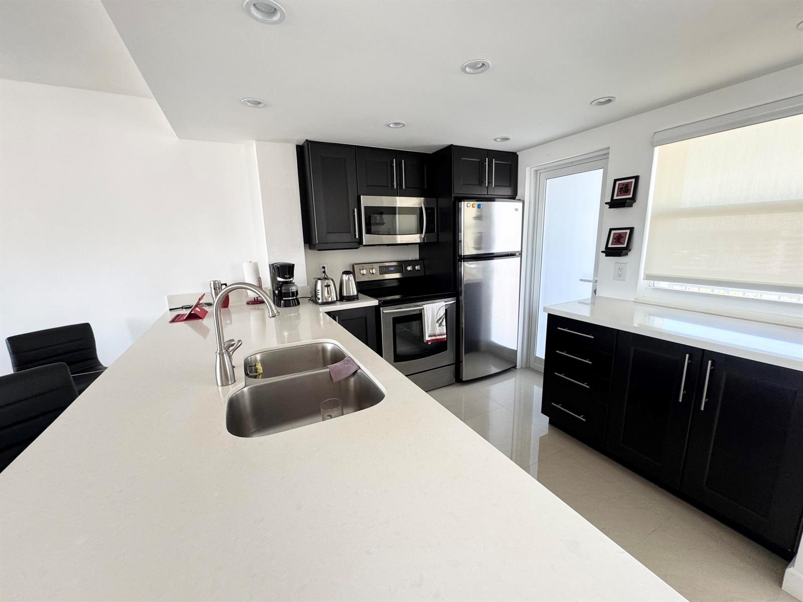 A kitchen features dark cabinets, stainless steel appliances, white countertops, and light tile flooring — 201 N Ocean Boulevard, Pompano Beach FL 33062, POMPANO BEACH, FL