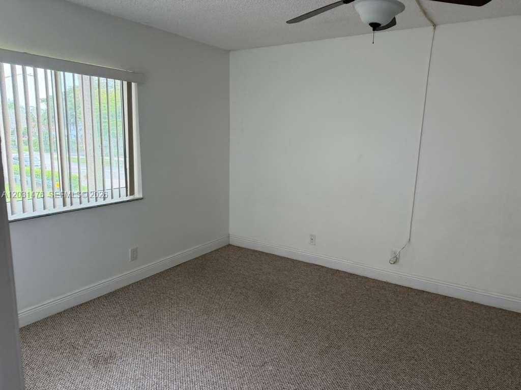 An empty bedroom features beige carpeting, white walls, a window with blinds, and a ceiling fan — 140 Lakeview Dr # 211, Weston FL 33326, WESTON, FL