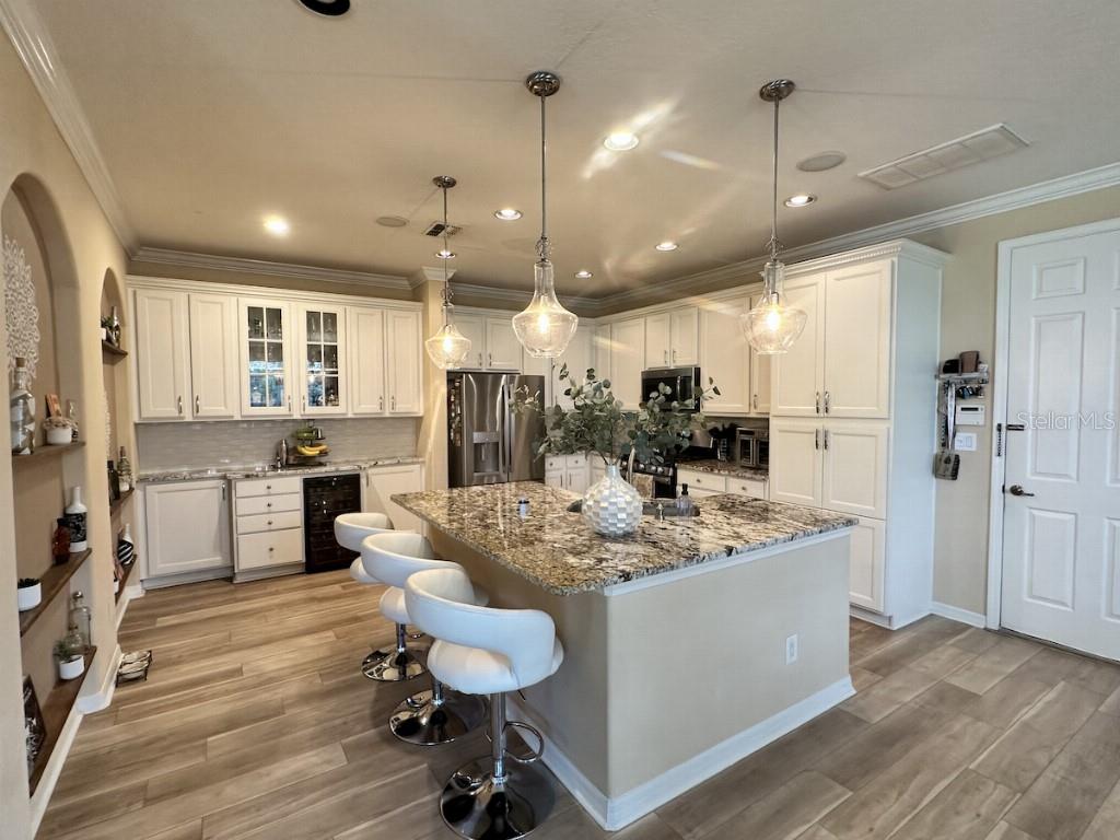 A kitchen with white cabinets, granite countertops, a central island with bar stools, and wood-look flooring — 11107 GREEN PARK CIRCLE, TAMPA, FL