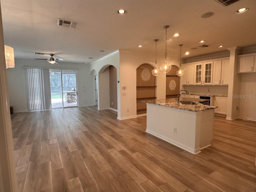 An open-concept kitchen and living area featuring light wood flooring, white cabinetry, and granite countertops — 11107 GREEN PARK CIRCLE, TAMPA, FL