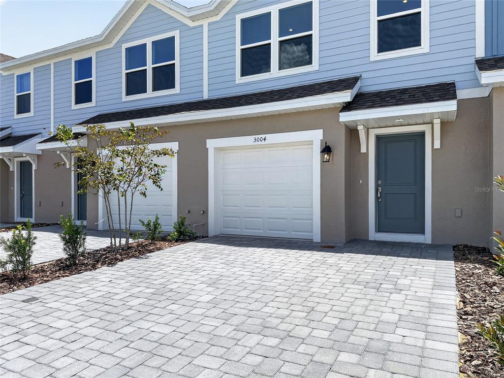 A two-story townhouse exterior features light blue siding, a tan stucco base, and a paver driveway — 3004 JESSAMINE DRIVE, TAVARES, FL