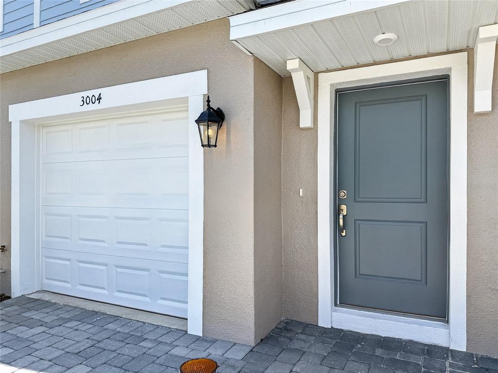 A tan exterior wall features a white garage door, a gray front door, and lighting — 3004 JESSAMINE DRIVE, TAVARES, FL