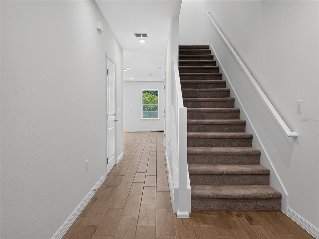 A hallway with wood-look tile flooring leads to a staircase with brown carpet — 3004 JESSAMINE DRIVE, TAVARES, FL