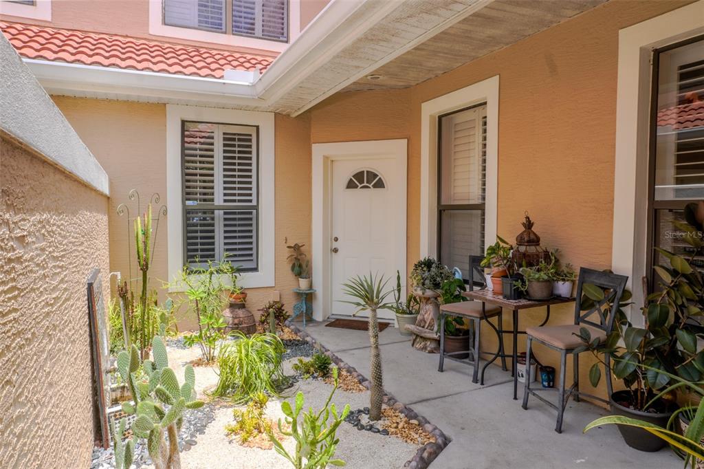 A courtyard entrance features a white door, a small bistro set, and various potted plants — 1010 WINDERLEY PLACE UNIT 149, MAITLAND, FL