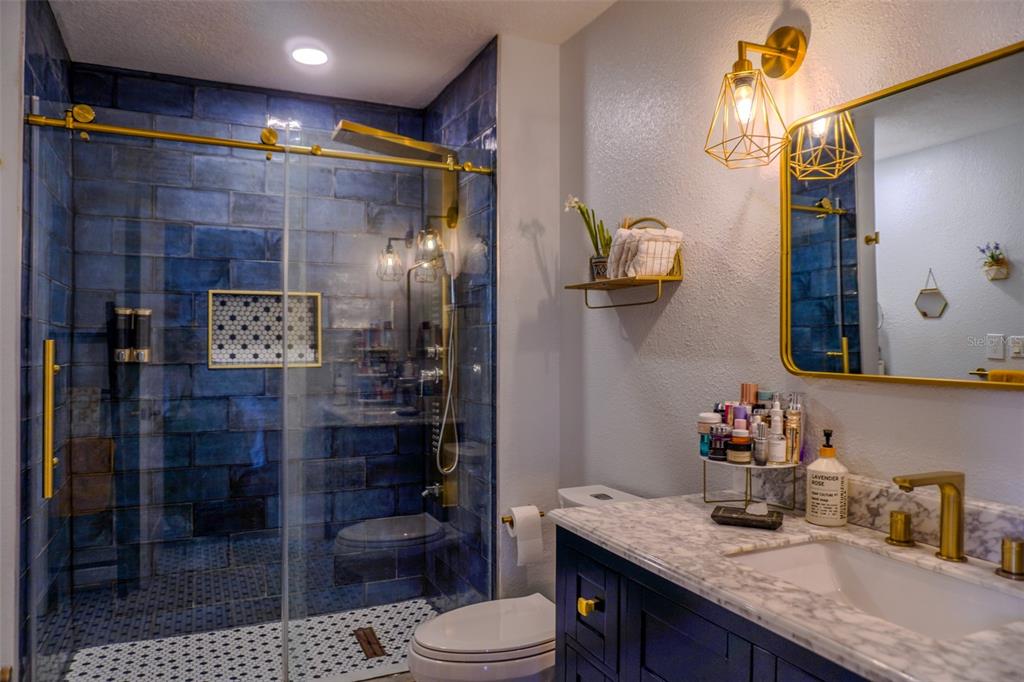 A bathroom features a blue-tiled walk-in shower, a marble vanity, and gold-toned fixtures — 1010 WINDERLEY PLACE UNIT 149, MAITLAND, FL