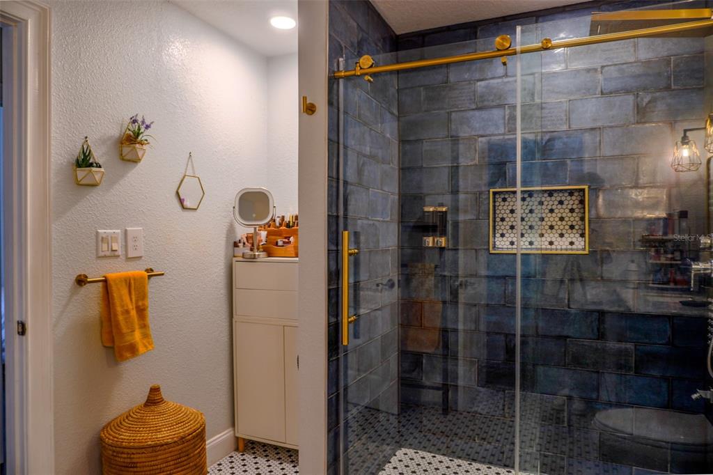A bathroom features a glass-enclosed shower with blue subway tiles and gold hardware — 1010 WINDERLEY PLACE UNIT 149, MAITLAND, FL