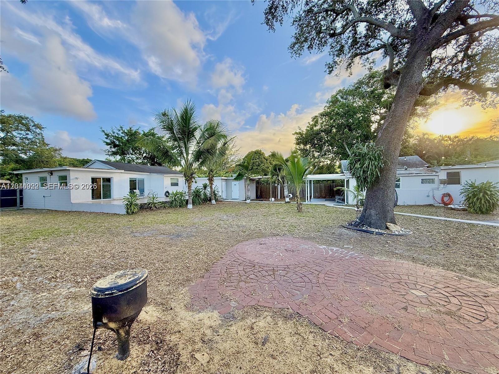 A backyard features a brick patio, a large tree, and white single-story buildings — 947 NE 149th St, Miami FL 33161, MIAMI, FL