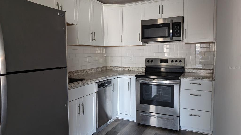 A kitchen features white cabinets, stainless steel appliances, granite countertops, and a subway tile backsplash — 3924 SW 26TH DRIVE UNIT 6, GAINESVILLE, FL
