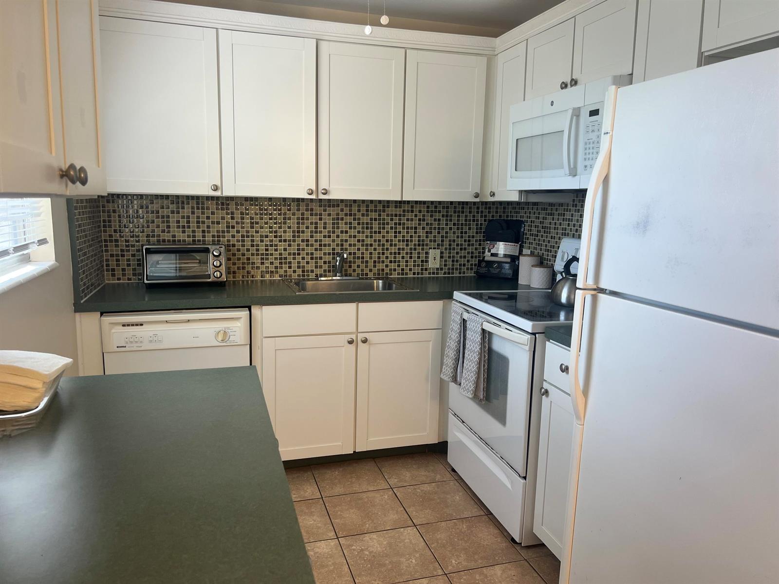 A kitchen with white cabinets, green countertops, a tiled backsplash, and white appliances — 318 Mansfield H, Boca Raton FL 33434, BOCA RATON, FL