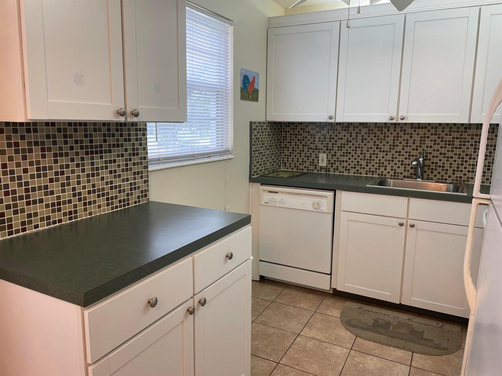 A kitchen features white cabinets, dark countertops, a mosaic tile backsplash, and tile flooring — 318 Mansfield H, Boca Raton FL 33434, BOCA RATON, FL