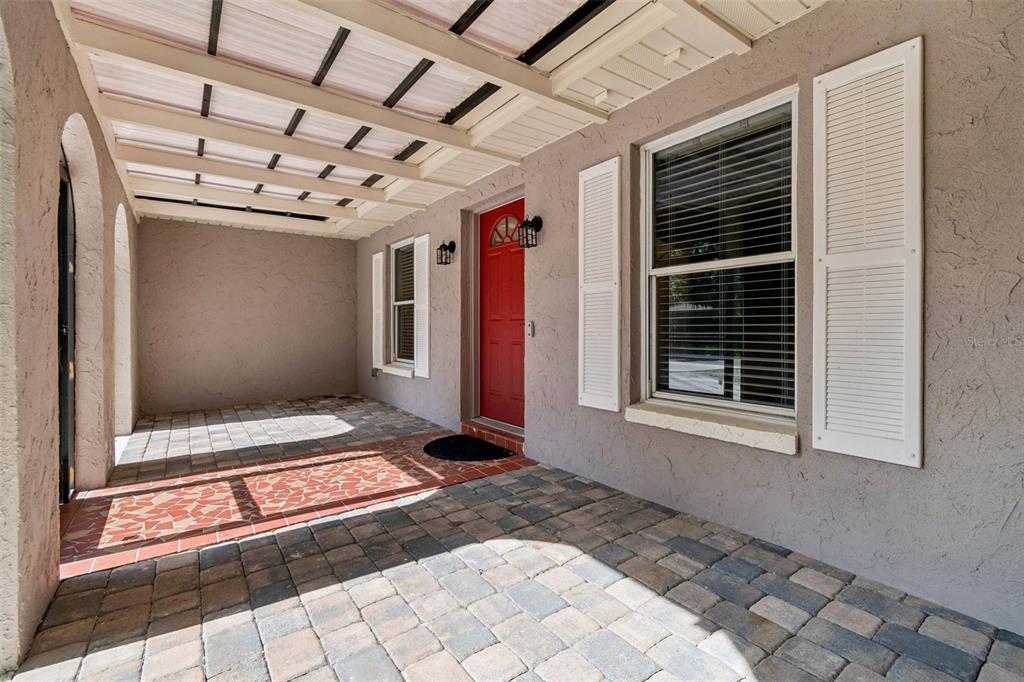 A covered patio features paver flooring, a red front door, and white window shutters — 503 ROLLINGVIEW DRIVE, TEMPLE TERRACE, FL