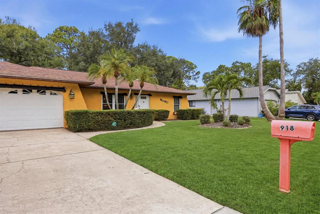 A yellow single-story house with a white garage door, palm trees, and a red mailbox — 918 ELL WAY, SARASOTA, FL
