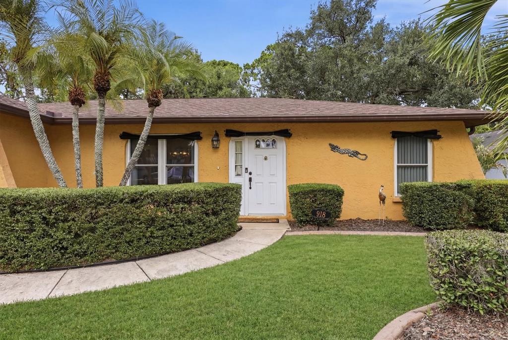 A yellow single-story house features a white front door, a walkway, and manicured hedges — 918 ELL WAY, SARASOTA, FL