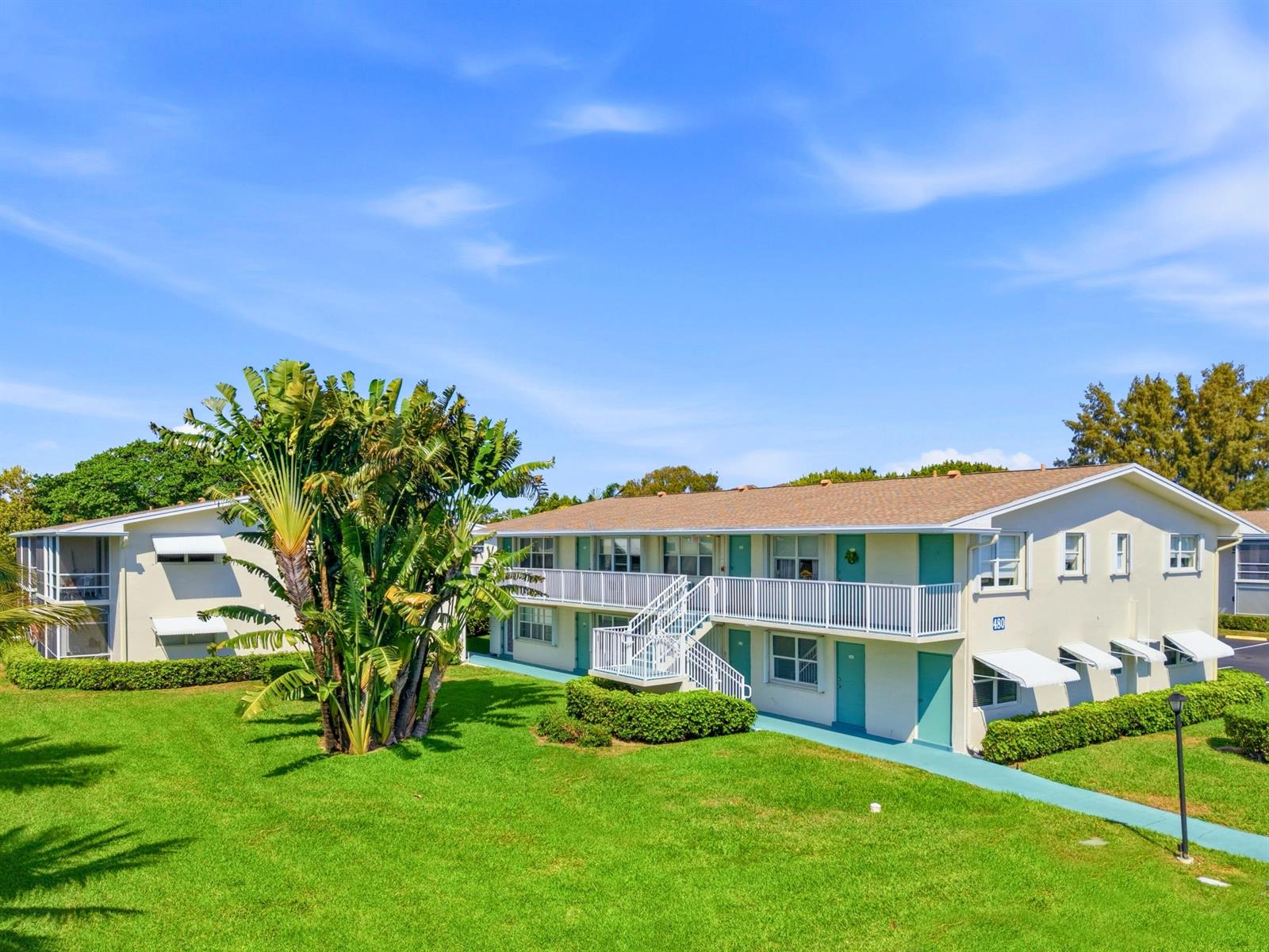 A two-story apartment building features a white exterior, teal doors, and a large tropical plant — 480 Horizons W # 208, Boynton Beach FL 33435, BOYNTON BEACH, FL