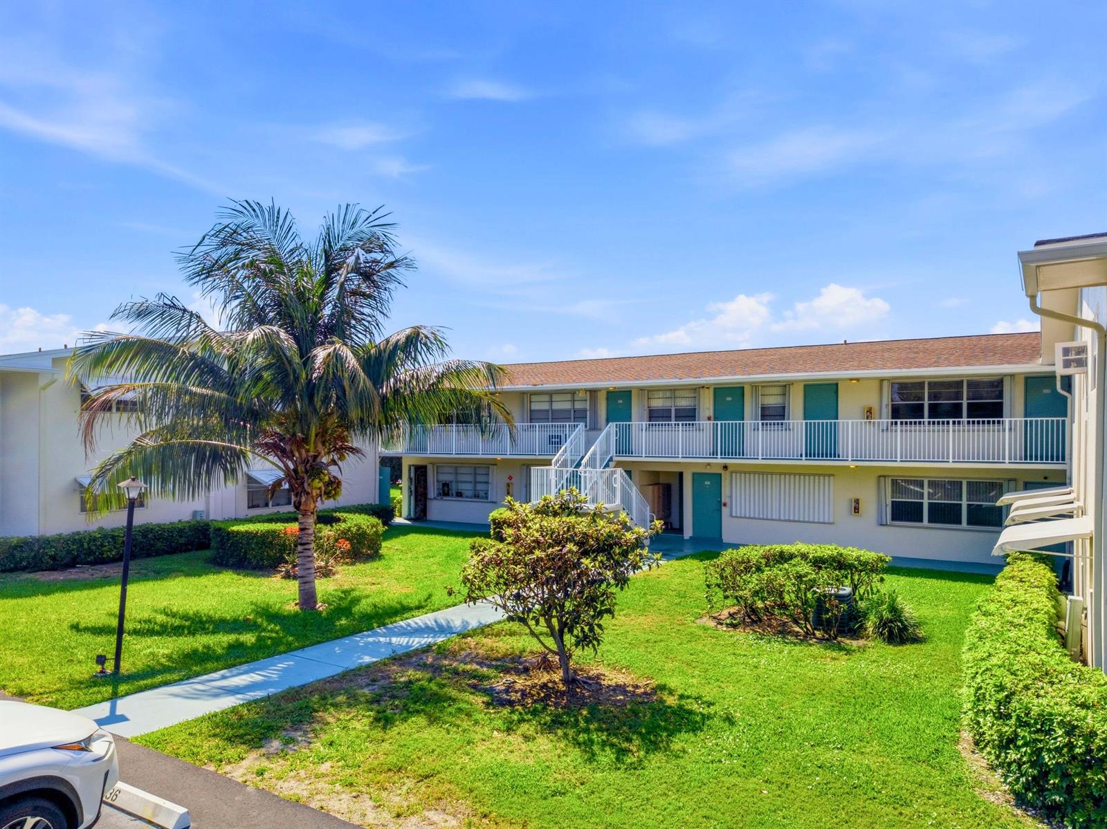 A two-story apartment building with a grassy courtyard, palm tree, and exterior staircases — 480 Horizons W # 208, Boynton Beach FL 33435, BOYNTON BEACH, FL