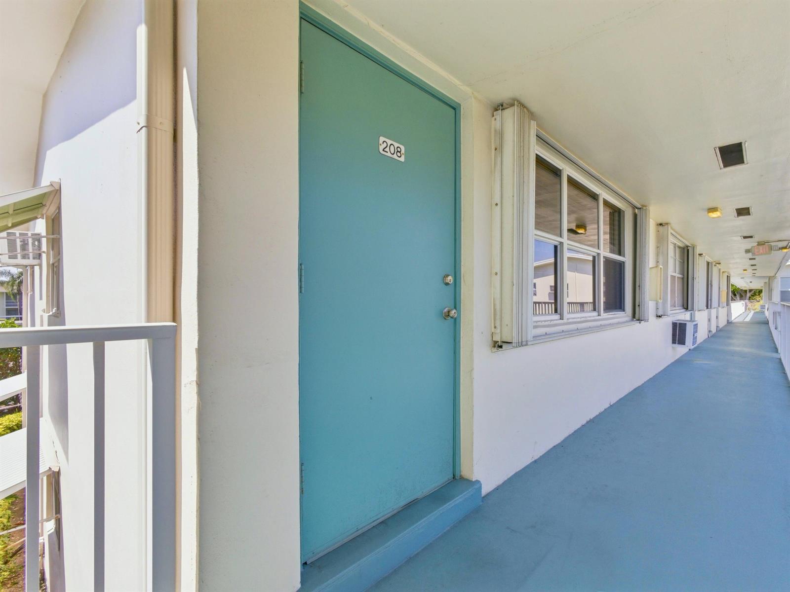 An exterior view of a teal apartment door labeled 208 along an open-air hallway — 480 Horizons W # 208, Boynton Beach FL 33435, BOYNTON BEACH, FL