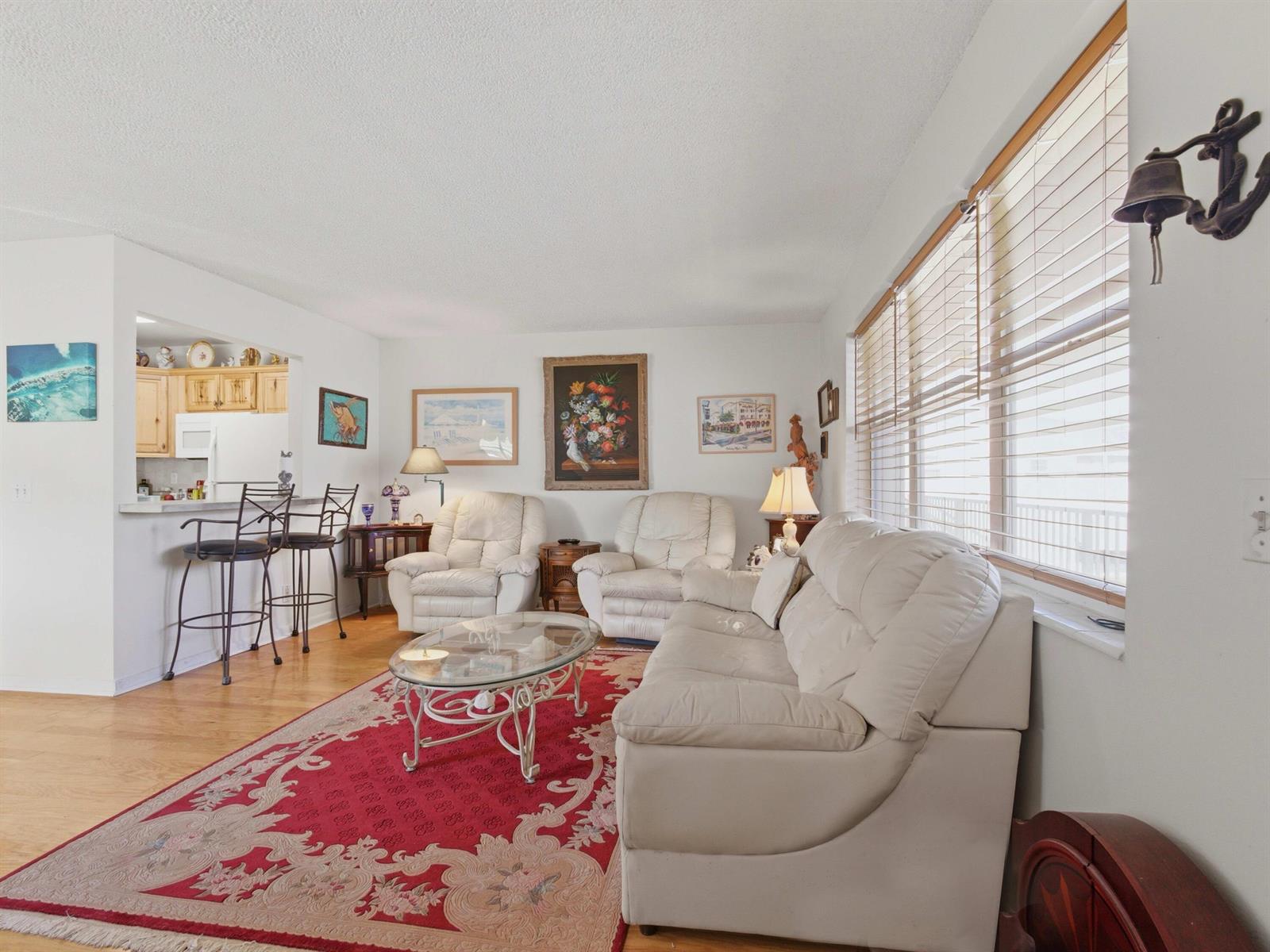 A living room with white leather furniture, a red patterned rug, and a kitchen pass-through — 480 Horizons W # 208, Boynton Beach FL 33435, BOYNTON BEACH, FL