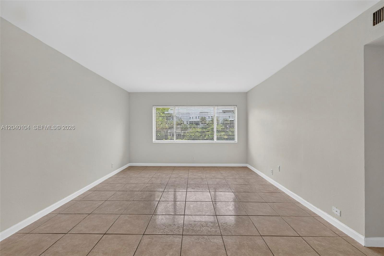 An empty room features beige walls, large square floor tiles, and a single window — 151 SE 6th Ave # 16, Pompano Beach FL 33060, POMPANO BEACH, FL