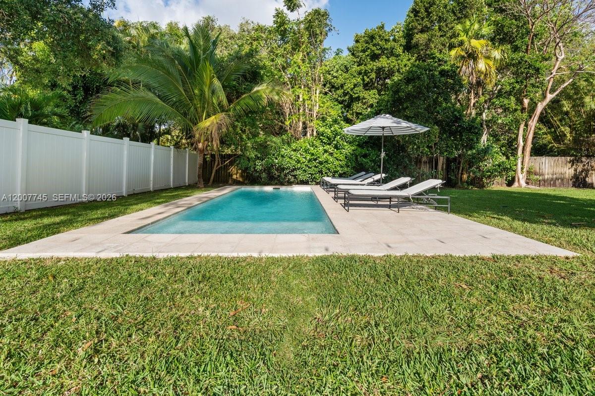 A rectangular swimming pool with lounge chairs and an umbrella sits in a grassy backyard — 11790 NE 8th Ave, Biscayne Park FL 33161, BISCAYNE PARK, FL