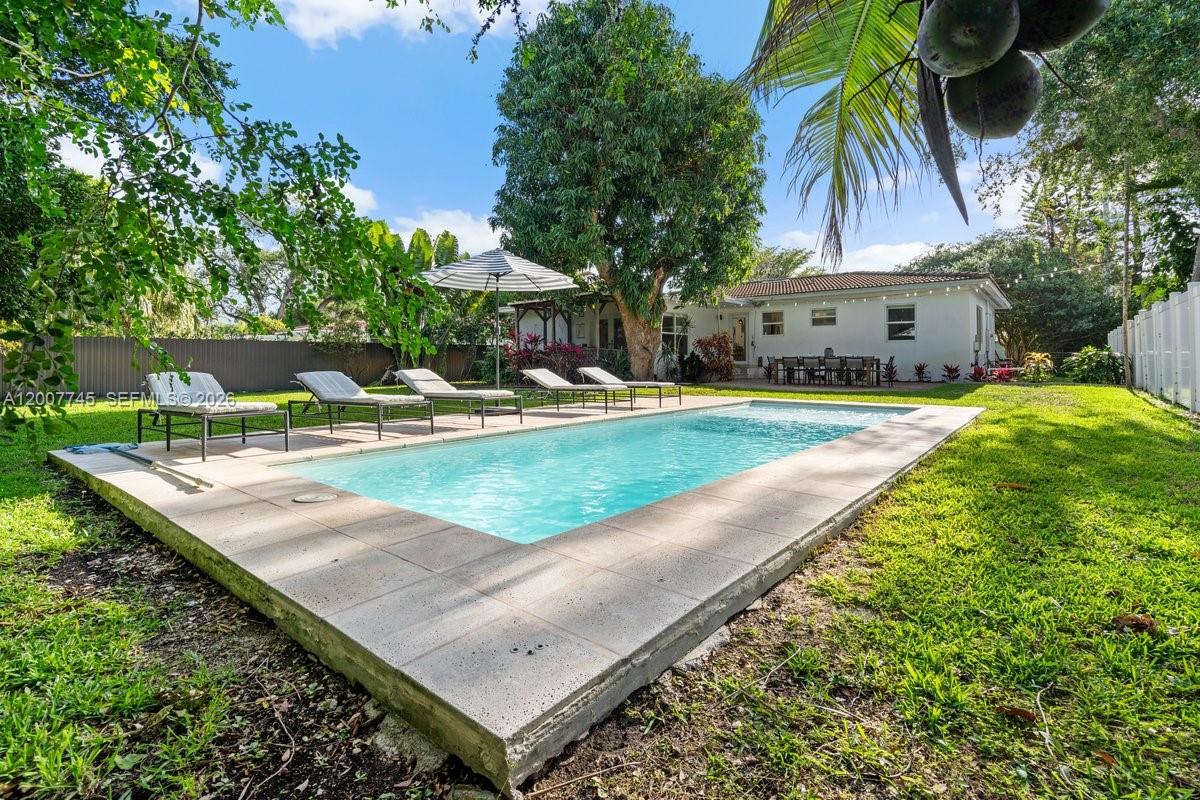 A rectangular swimming pool sits in a grassy backyard with lounge chairs and a house — 11790 NE 8th Ave, Biscayne Park FL 33161, BISCAYNE PARK, FL