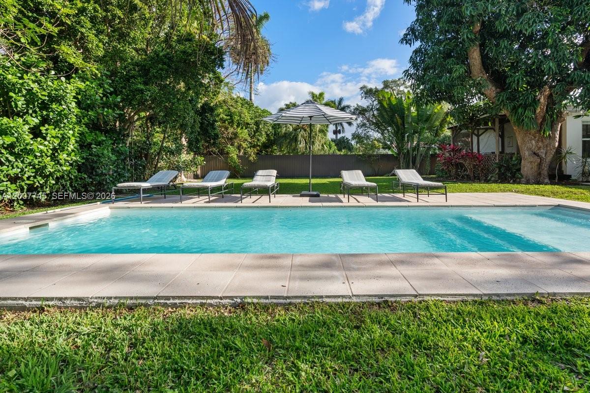 A rectangular swimming pool sits in a backyard with lounge chairs and a striped umbrella — 11790 NE 8th Ave, Biscayne Park FL 33161, BISCAYNE PARK, FL