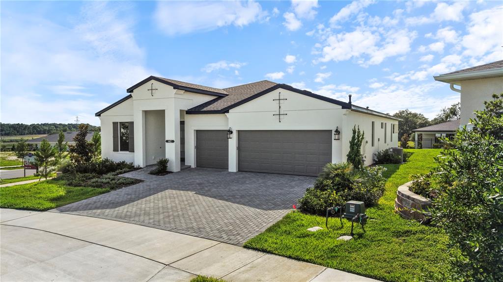 A single-story house with a white stucco exterior, a gray three-car garage, and a paver driveway — 442 TURIN WAY, LADY LAKE, FL