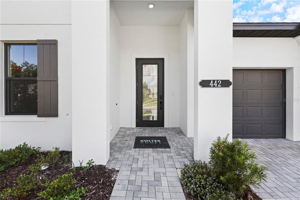 The exterior of a modern home features a paved walkway leading to a dark front door — 442 TURIN WAY, LADY LAKE, FL