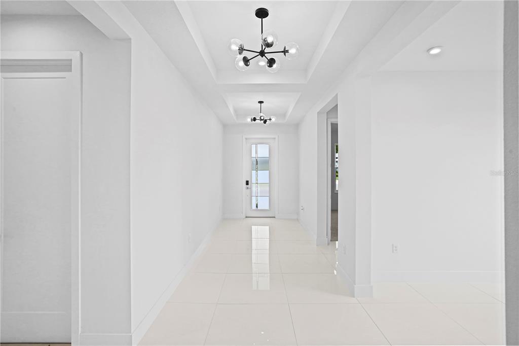 A bright hallway features white tile floors, recessed tray ceilings, and two modern globe chandeliers — 442 TURIN WAY, LADY LAKE, FL
