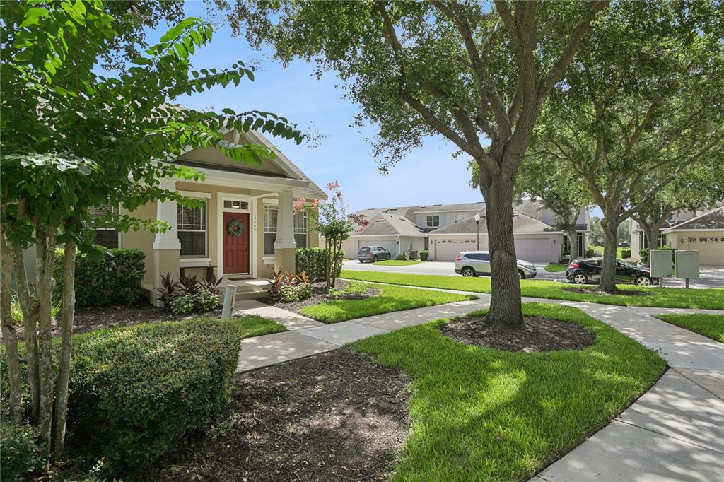 A tan house with a red front door sits beside a sidewalk and large trees — 13449 CARROWAY STREET, WINDERMERE, FL