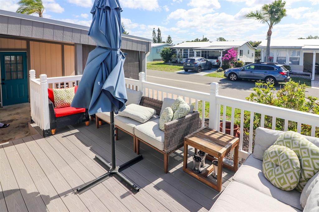 A wooden deck features outdoor furniture, a closed umbrella, and a white railing overlooking a street — 2100 KINGS HIGHWAY UNIT 662, PORT CHARLOTTE, FL