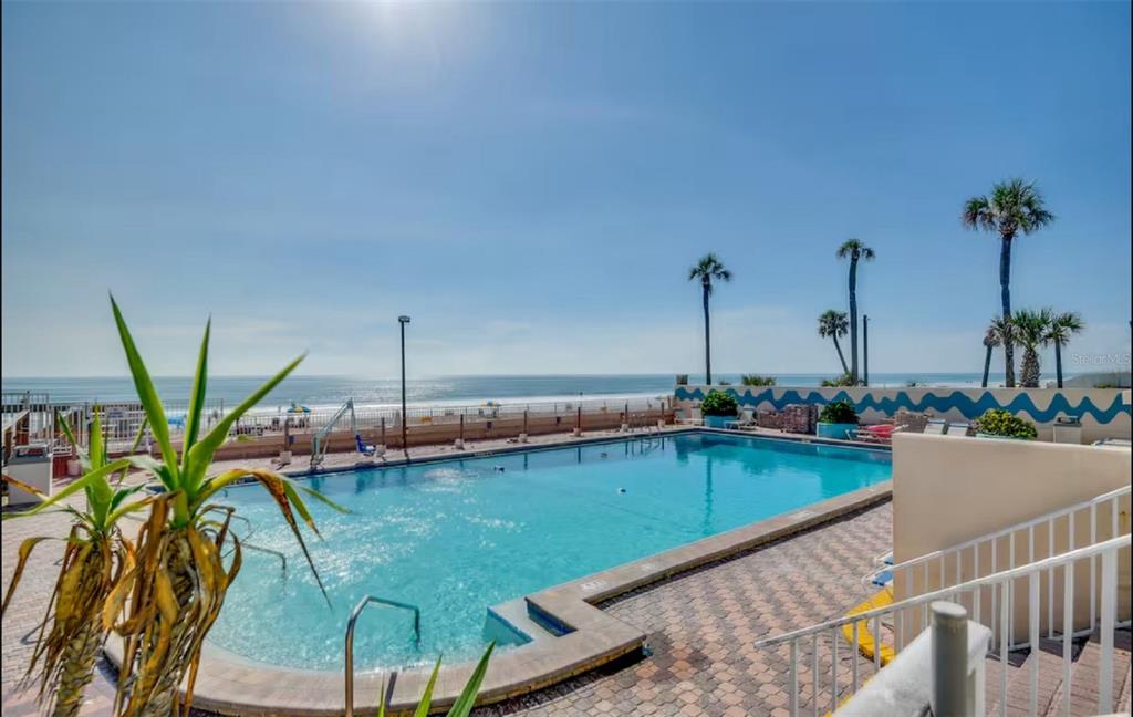 An outdoor swimming pool overlooks the ocean with a paved deck and palm trees — 313 S ATLANTIC AVENUE UNIT 4100, DAYTONA BEACH, FL