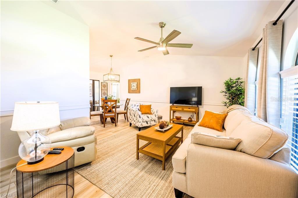 A living room with light wood flooring, a beige sofa, and a dining area beyond — 420 SW 37TH STREET, CAPE CORAL, FL