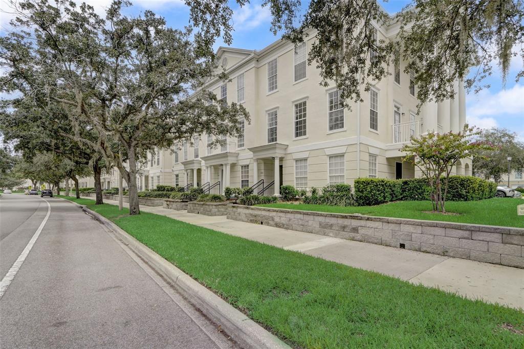 A multi-story cream-colored building with a sidewalk, lawn, and large trees in the foreground — 236 CELEBRATION BOULEVARD UNIT 236, CELEBRATION, FL