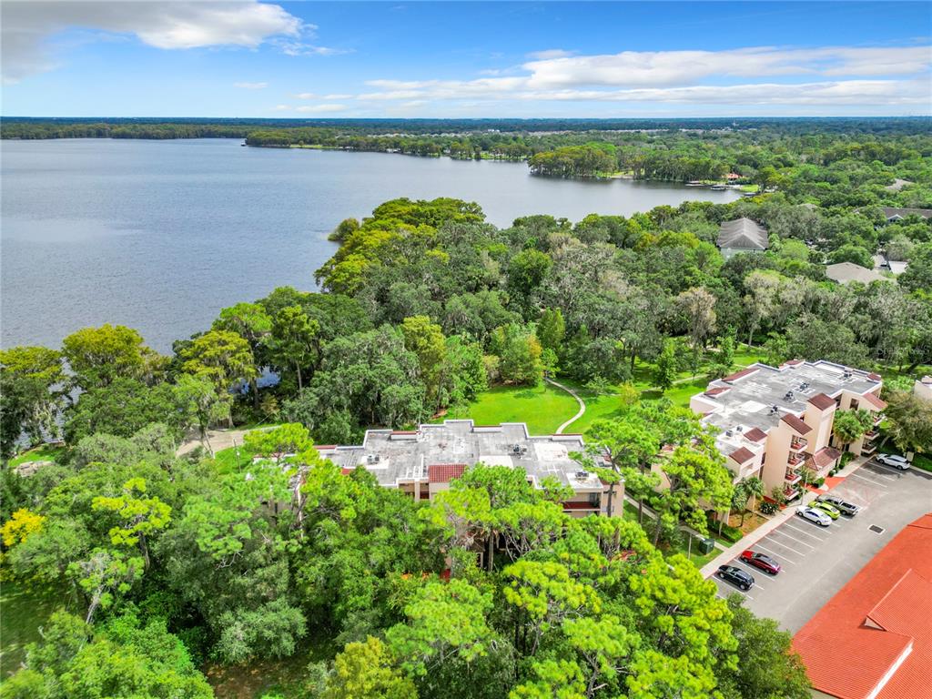 An aerial view shows multi-story apartment buildings nestled among trees next to a large lake — 1158 CARMEL CIRCLE UNIT 430, CASSELBERRY, FL