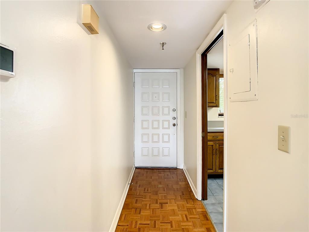 A hallway with parquet flooring leads to a white door and an adjacent kitchen doorway — 1158 CARMEL CIRCLE UNIT 430, CASSELBERRY, FL