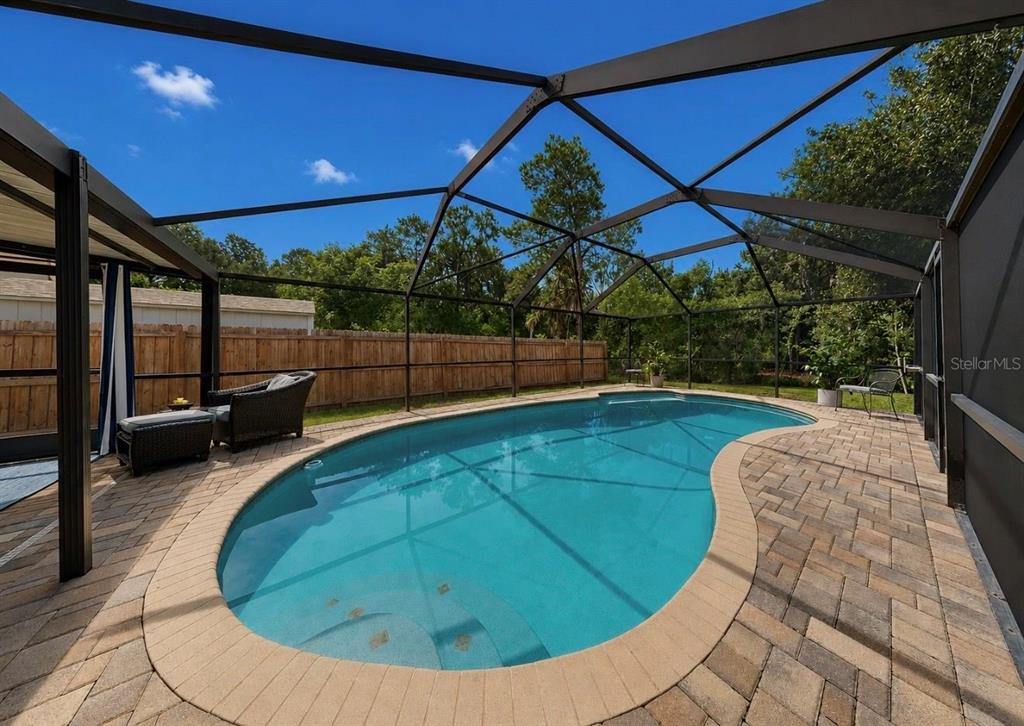 A screened-in swimming pool with a paver deck and a wooden privacy fence — 1005 HIGHGROVE COURT, VALRICO, FL