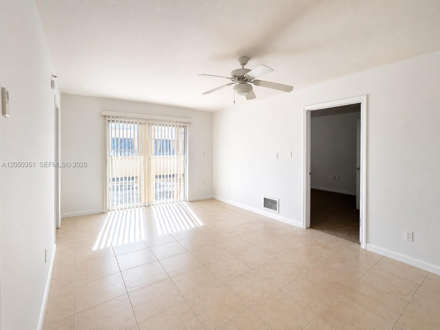 An empty room features beige tile flooring, a ceiling fan, and a sliding glass door — 2415 NW 16th St Rd # 1, Miami FL 33125, MIAMI, FL