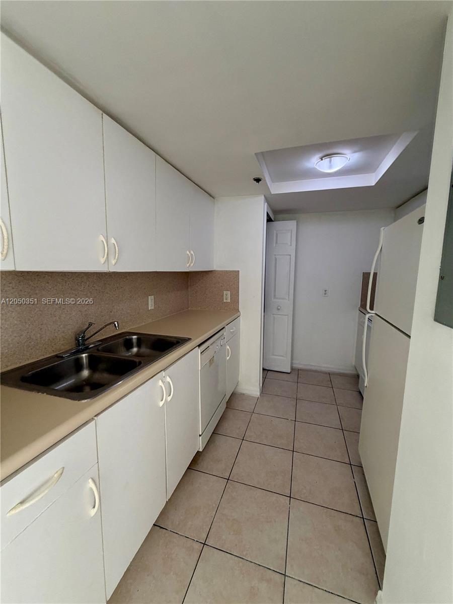 A galley-style kitchen features white cabinets, a double sink, and a white refrigerator — 2415 NW 16th St Rd # 1, Miami FL 33125, MIAMI, FL