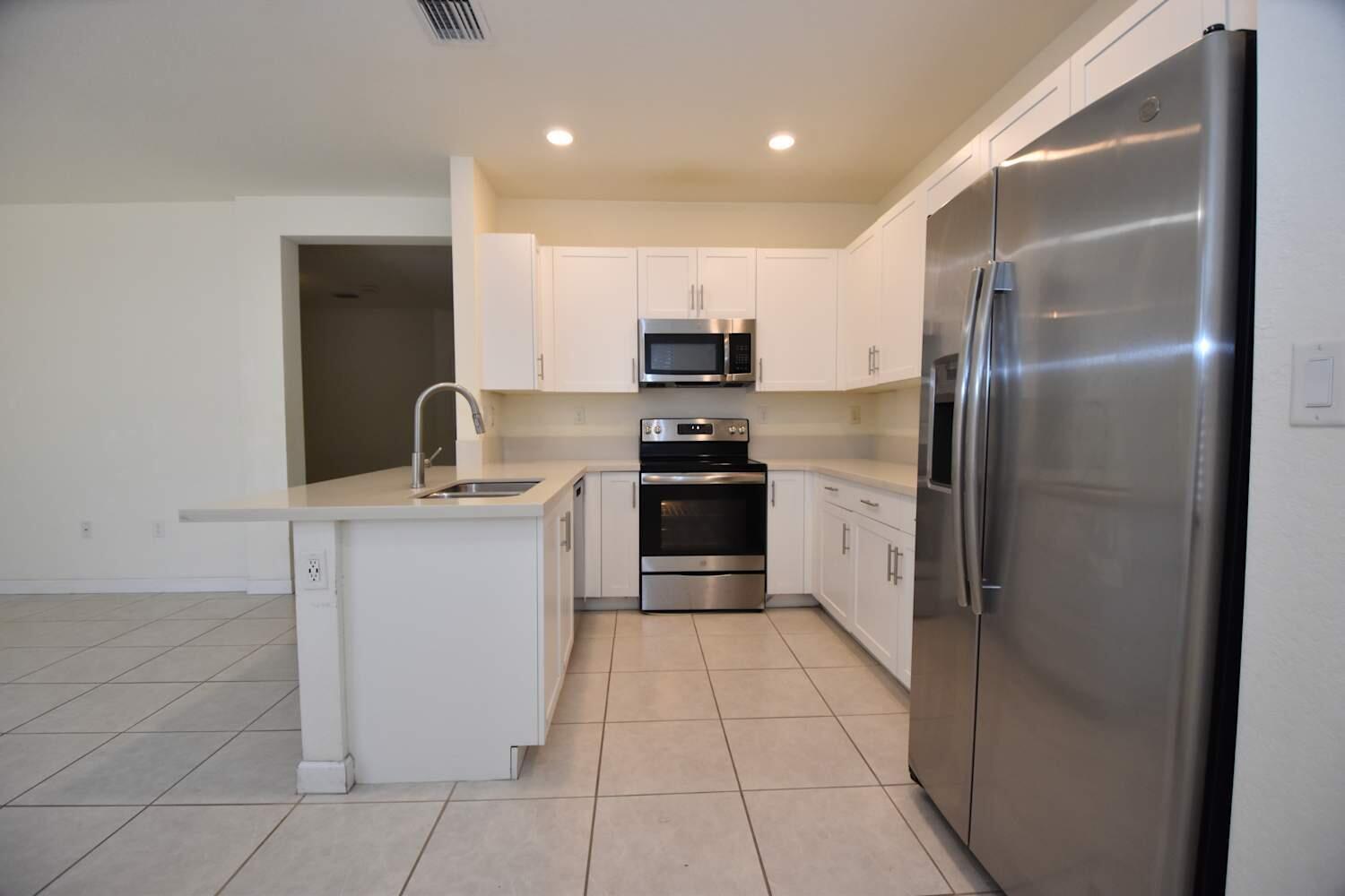A kitchen with white cabinets, stainless steel appliances, and a central island with a sink — HIALEAH, FL
