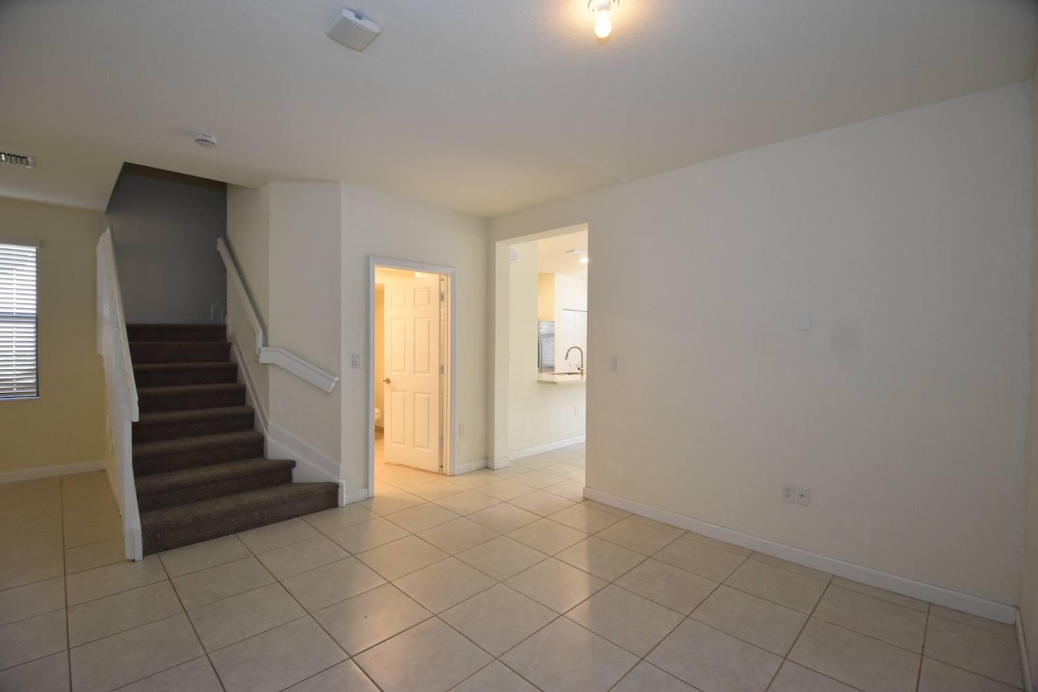 An interior view shows a tiled room with a staircase, a doorway, and a kitchen pass-through — HIALEAH, FL