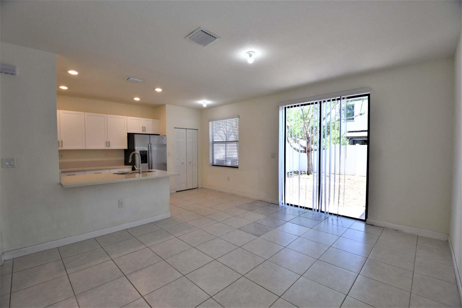 A kitchen with white cabinets and a breakfast bar opens into a tiled living area — HIALEAH, FL