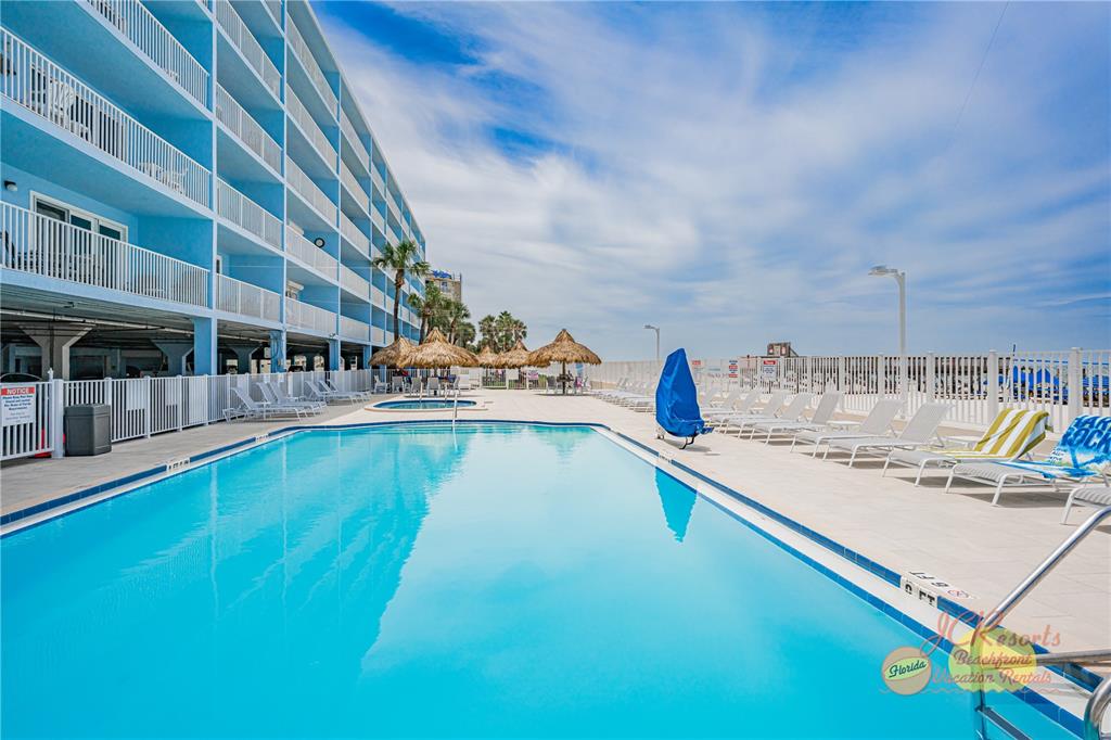 A swimming pool sits on a patio next to a multi-story blue hotel building — 18500 GULF BOULEVARD UNIT 404, INDIAN SHORES, FL