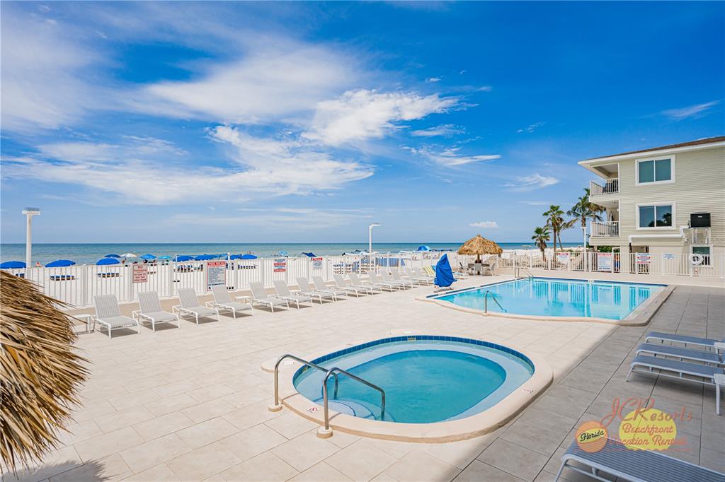 An outdoor pool and hot tub area overlook the beach with lounge chairs and fencing — 18500 GULF BOULEVARD UNIT 404, INDIAN SHORES, FL