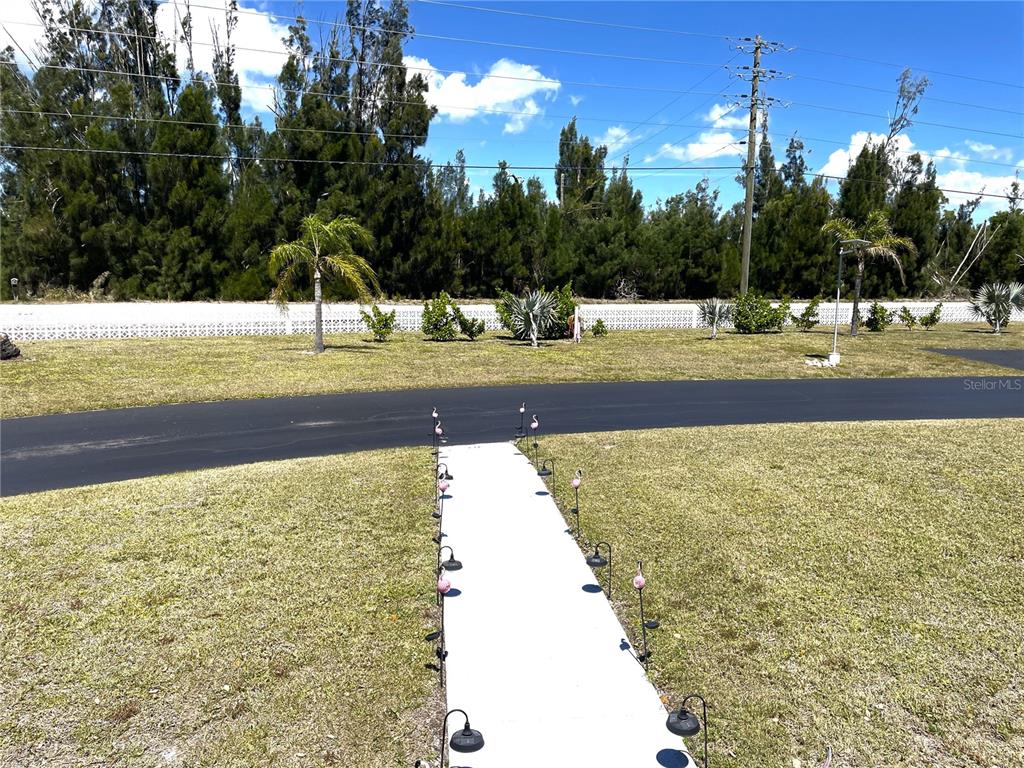 A paved walkway lined with small flamingo ornaments leads across a lawn toward a driveway — 24437 HARBORVIEW ROAD UNIT 70, PORT CHARLOTTE, FL