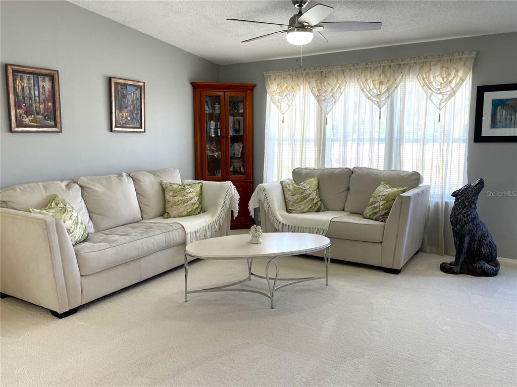 A living room features two beige sofas, a coffee table, and a corner display cabinet — 24437 HARBORVIEW ROAD UNIT 70, PORT CHARLOTTE, FL