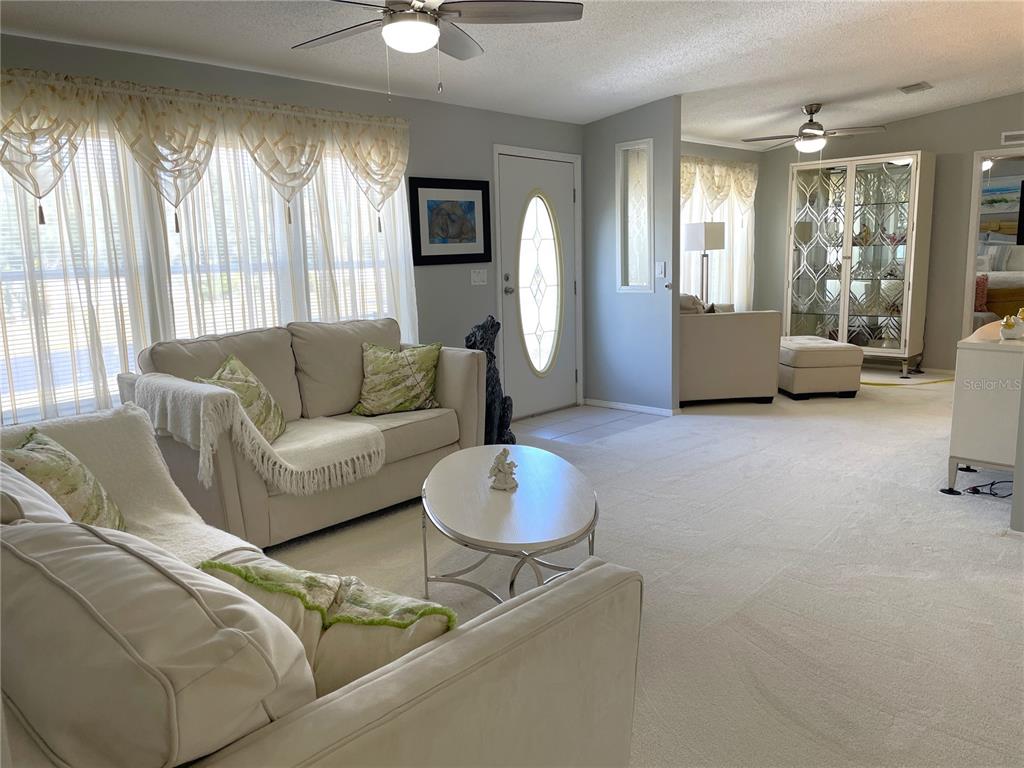 A living room features light-colored furniture, white carpeting, and a glass-front display cabinet — 24437 HARBORVIEW ROAD UNIT 70, PORT CHARLOTTE, FL