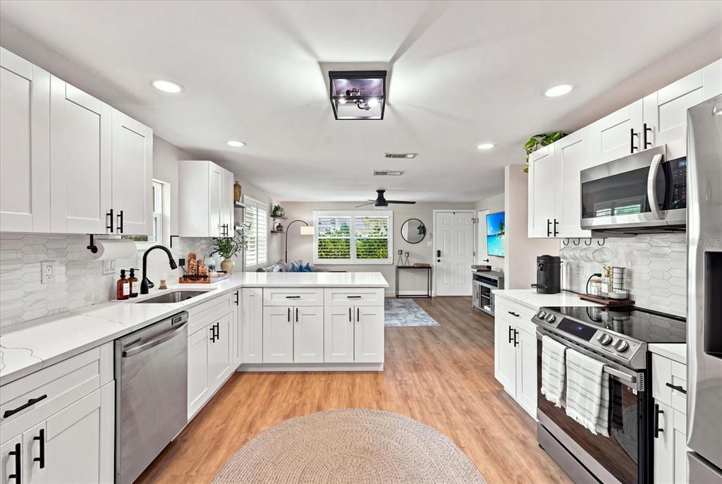A bright kitchen features white cabinets, stainless steel appliances, and wood-look flooring — 2449 WOOD STREET, SARASOTA, FL
