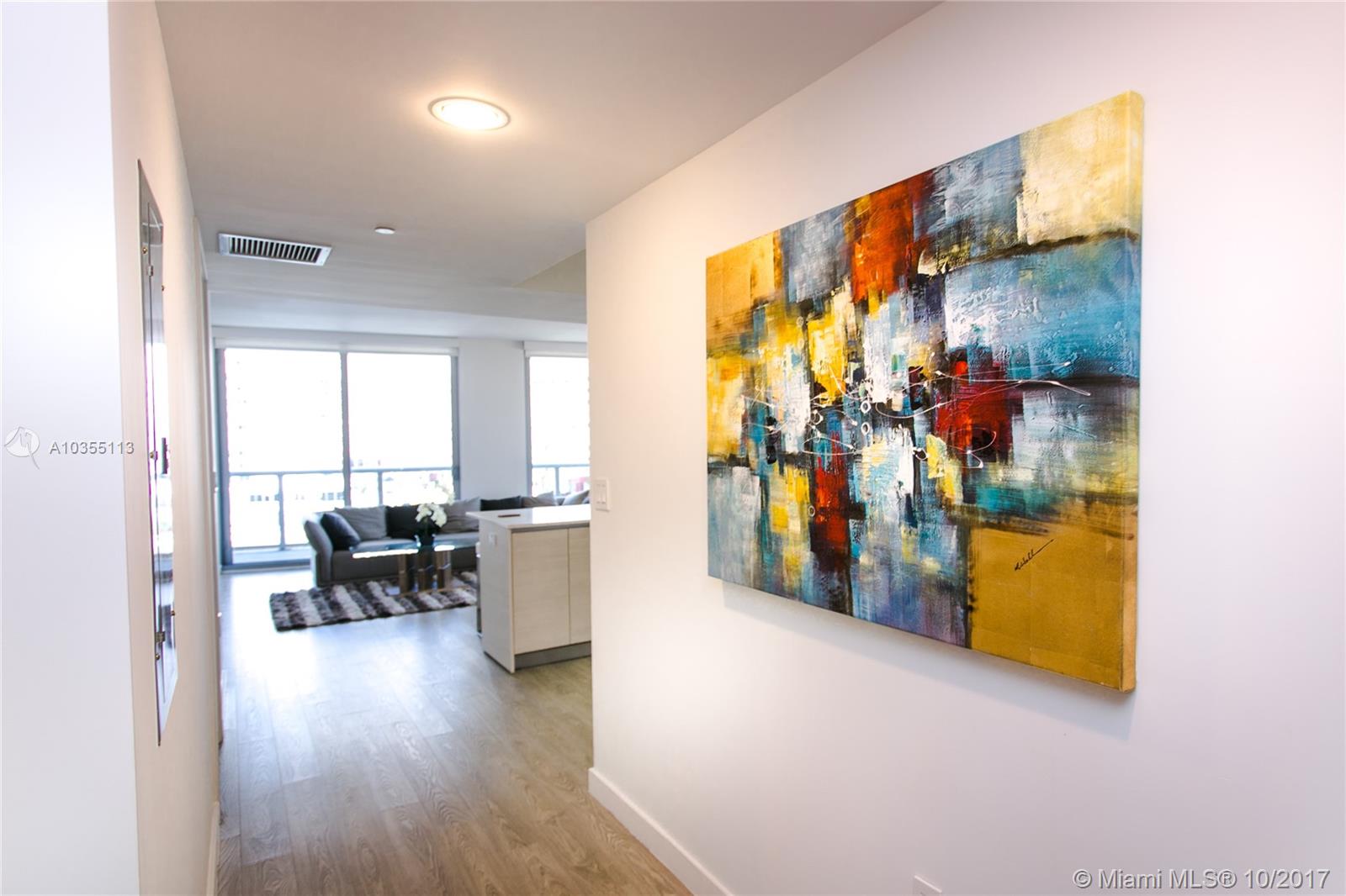 A hallway with a large abstract painting leads to an open-concept living area with windows — 2600 E Hallandale Beach Blvd, Hallandale Beach FL 33009, HALLANDALE BEACH, FL